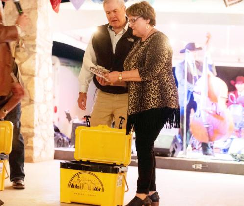 LEFT- KRTC Ranches’ Denzil and Kathy West open the cooler they won at auction Friday night. After all 3 coolers were auctioned, buyers opened them simultaneously to reveal the prize inside. The West’s cooler contained cash. The other 2 had a local beef package, and a ladies assortment basket. Sandy Kothmann, photo. BELOW- Library board member Laressa Brown displays the coveted Golden Ticket during its intense auction. Photo by Sandy Kothmann.