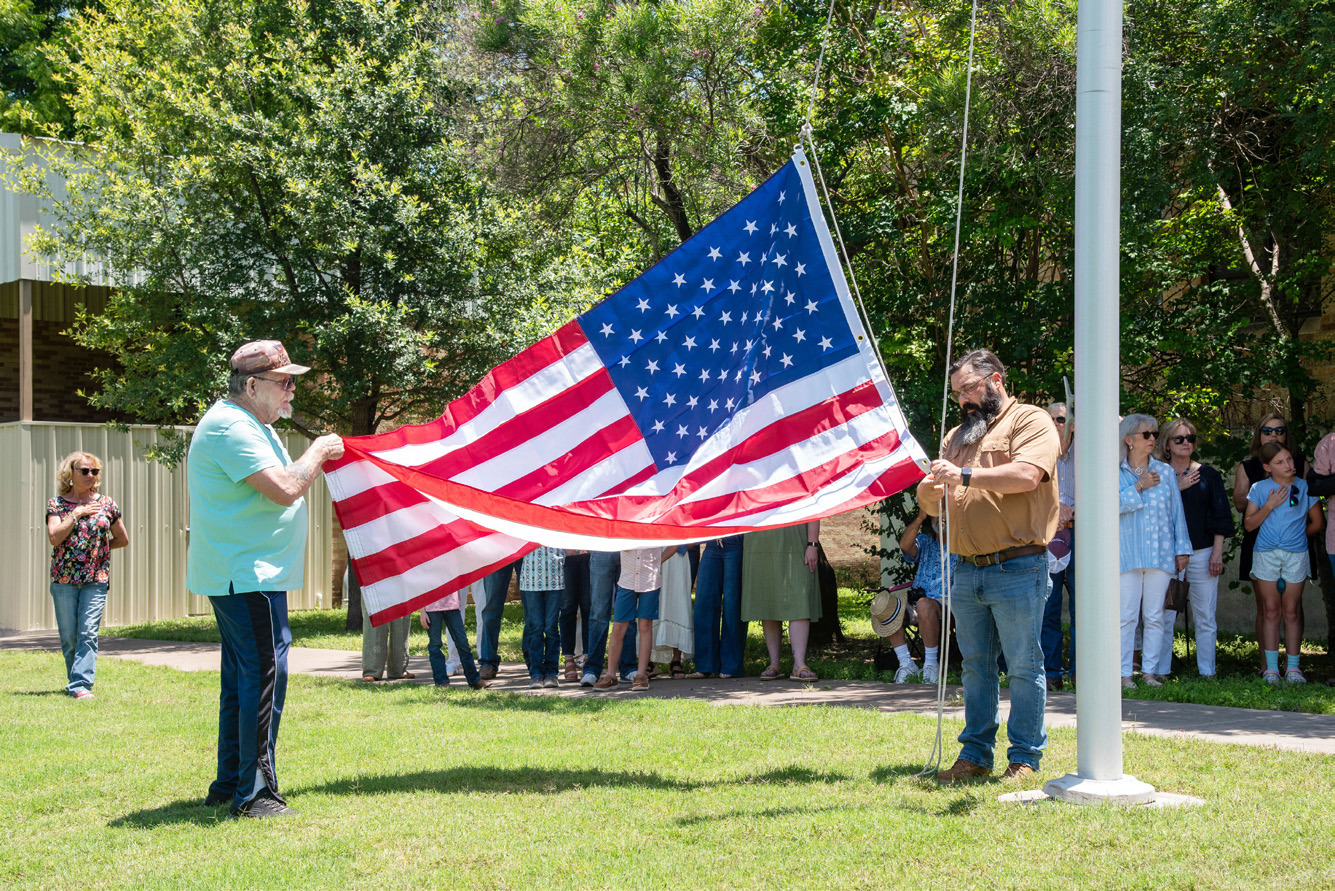 County Commissioner Ed Keith and Veterans Services Officer Gary Cheek raise the commemorative flag at the county office plaque reveal at the courthouse last Friday. Nora Davis, photo.