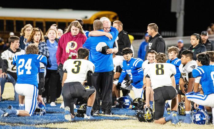 COMING TOGETHER is what communities do in times of loss. Prior to last Friday's district wrapup rivalry, Menard coach Jeff Campbell, center, accepted prayers and condolences from both sides of the field for the loss of his wife Debbra last week. The teams and spectators came together in prayer and remembrance both before and after the Yelowjacket win over Eden. Sandy Kothmann, photo.