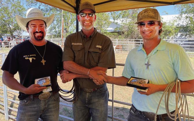 THE GOATS- Menard’s Michael Ramon, left, and Ty Titzman flank event announcer Tyler Wright, center, with their trophy belt buckles after the Hext Volunteer Fire Department Fish Fry fundraiser’s goat roping Saturday, October 1. TMN photo.