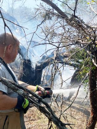 LEFT- Menard VFD's Jeff Whitson tends to a smoldering tree at a fire call near Hext last Friday. MVFD photo.