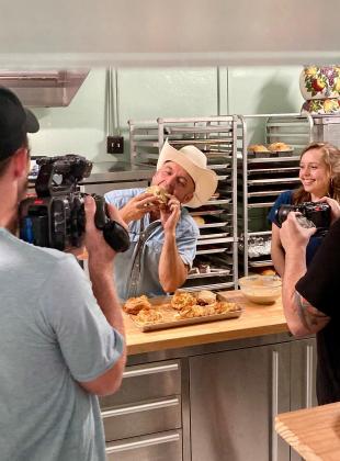 Maia Prest, far right, laughs as 'The Daytripper' Chet Garner enjoys a fresh-baked pastry during the film crew's visit to her family's bakery and market- Texas Scratch Kitchen in Menard. Courtesy photo.