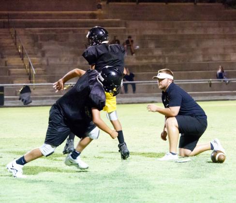 ABOVE- Jayden Payton and Eli Kothmann, both freshmen on this year’s Junior Varsity team, rep run plays with first year head coach and athletic director Bryson Oliver during their Midnight Madness practice early Saturday morning. Nora Davis, photo.