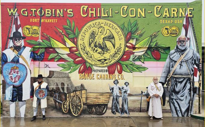 IT'S LIKE LOOKING IN A MIRROR kind of. Spanish Colonial Living Historians Gus Martinez, left as Soldado Josefo Vasquez, and Joe Gonzalez as fray Miguel de Molina (the only surviving Mission priest), right. These reenactors stand in front of their depictions in the Bud Menchaca mural that encompasses the south wall of The Menard Station on Frisco St. Courtesy photo. Contributed by Col. Terry Kelley, President, Presidio Restoration Corp.