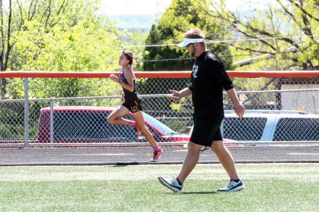 ON THE HOMESTRETCH- Danni Ruiz rounds the track during the Area track meet in Robert Lee. Under the watchful guidance of coach Bryson Oliver, also pictured, the freshman regional champion Ruiz will compete in both the 400m and 800m races at the state track meet next month. Nora Davis, photo.