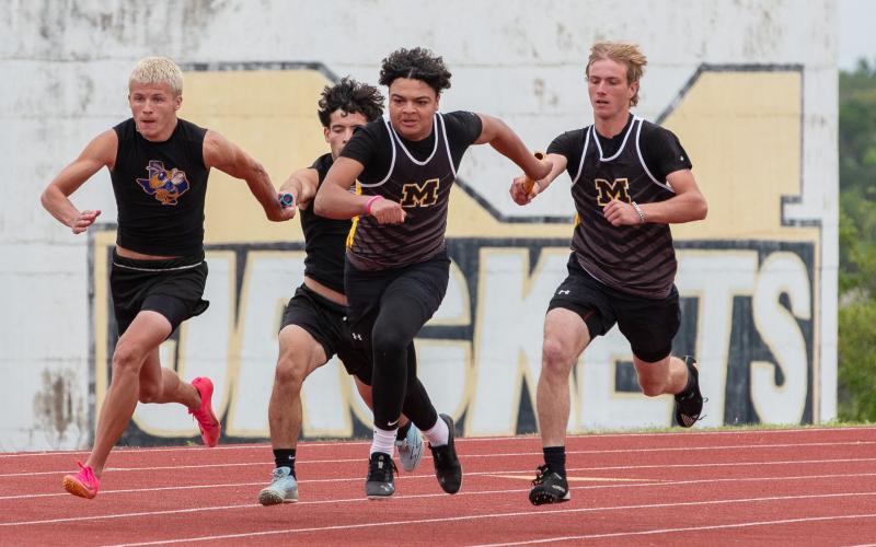 ABOVE- Neck in neck with Rochelle, third relay leg Tucker Pullen, far right, hands off to anchor leg Jayden Payton to finish the sprint relay at the district meet in Menard last week.