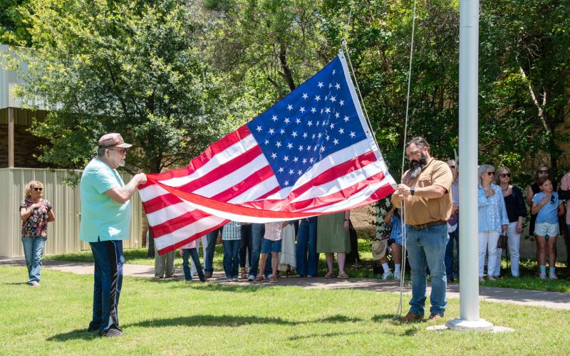 County Commissioner Ed Keith and Veterans Services Officer Gary Cheek raise the commemorative flag at the county office plaque reveal at the courthouse last Friday. Nora Davis, photo.