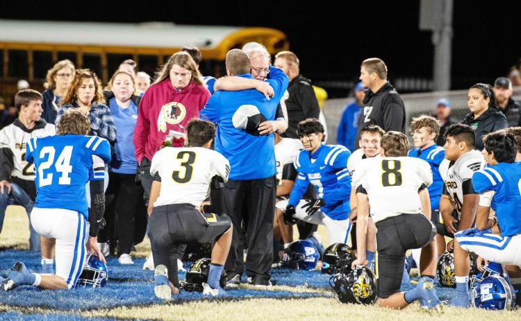 COMING TOGETHER is what communities do in times of loss. Prior to last Friday's district wrapup rivalry, Menard coach Jeff Campbell, center, accepted prayers and condolences from both sides of the field for the loss of his wife Debbra last week. The teams and spectators came together in prayer and remembrance both before and after the Yelowjacket win over Eden. Sandy Kothmann, photo.