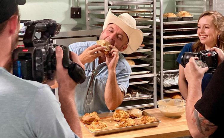 Maia Prest, far right, laughs as 'The Daytripper' Chet Garner enjoys a fresh-baked pastry during the film crew's visit to her family's bakery and market- Texas Scratch Kitchen in Menard. Courtesy photo.