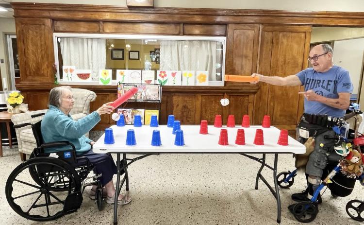 LEFT- There will always be something fun and stimulating going on for the residents of Menard Manor Skilled Nursing Facility if Activities Director Cheryl Spoons has anything to do with it, and she does! Pictured is Nellie Frnka and David Garza taking part in an activity using a “snowball” tied to a piece of pool noodle to work on hand-eye coordination by knocking down Solo cups. Manor residents enjoy a variety of games, activities, crafts and interaction year-round. Courtesy photo.