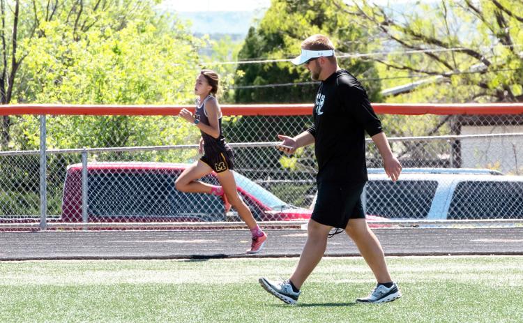ON THE HOMESTRETCH- Danni Ruiz rounds the track during the Area track meet in Robert Lee. Under the watchful guidance of coach Bryson Oliver, also pictured, the freshman regional champion Ruiz will compete in both the 400m and 800m races at the state track meet next month. Nora Davis, photo.
